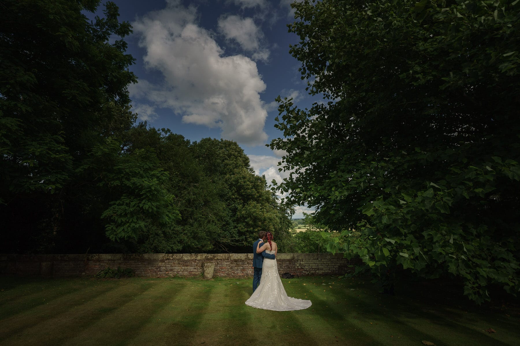 A bride and groom standing in the picturesque Pimhill Barn, Shropshire, under a cloudy sky.