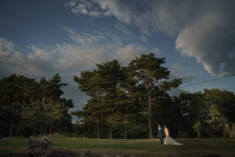 A bride and groom standing in a field at Pimhill Barn, Shropshire under a cloudy sky.