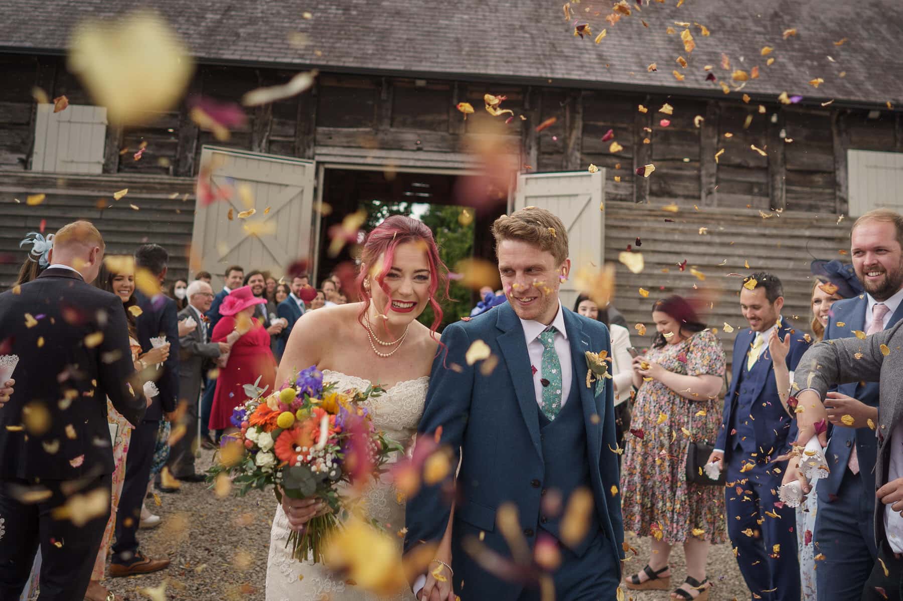 A bride and groom walk out of Pimhill Barn in Shropshire with confetti thrown at them.
