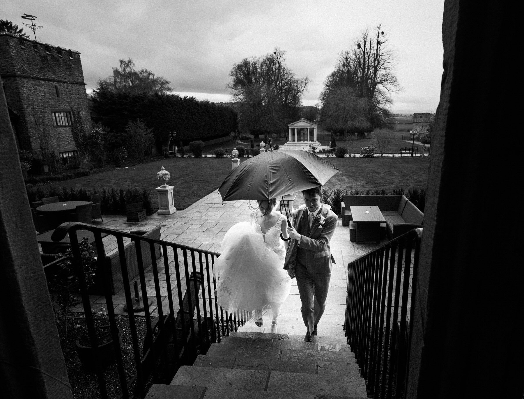 A bride and groom walking down the stairs at Rowton Castle Wedding, sheltered by an umbrella.