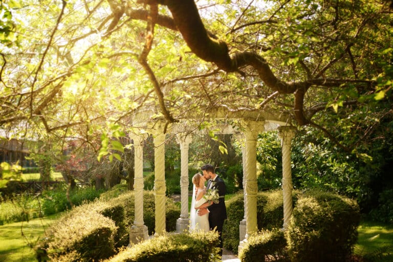 A bride and groom standing under a gazebo in the beautiful gardens of Mill Barns Wedding venue.