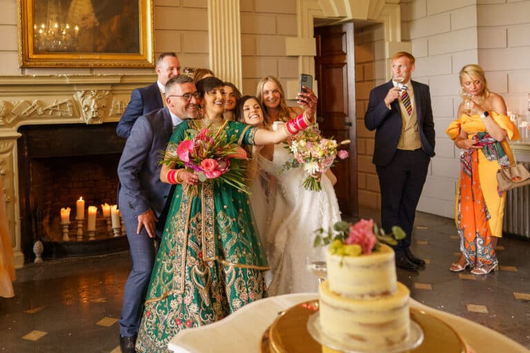 A group of people posing for a wedding photo in front of a cake at Davenport House.