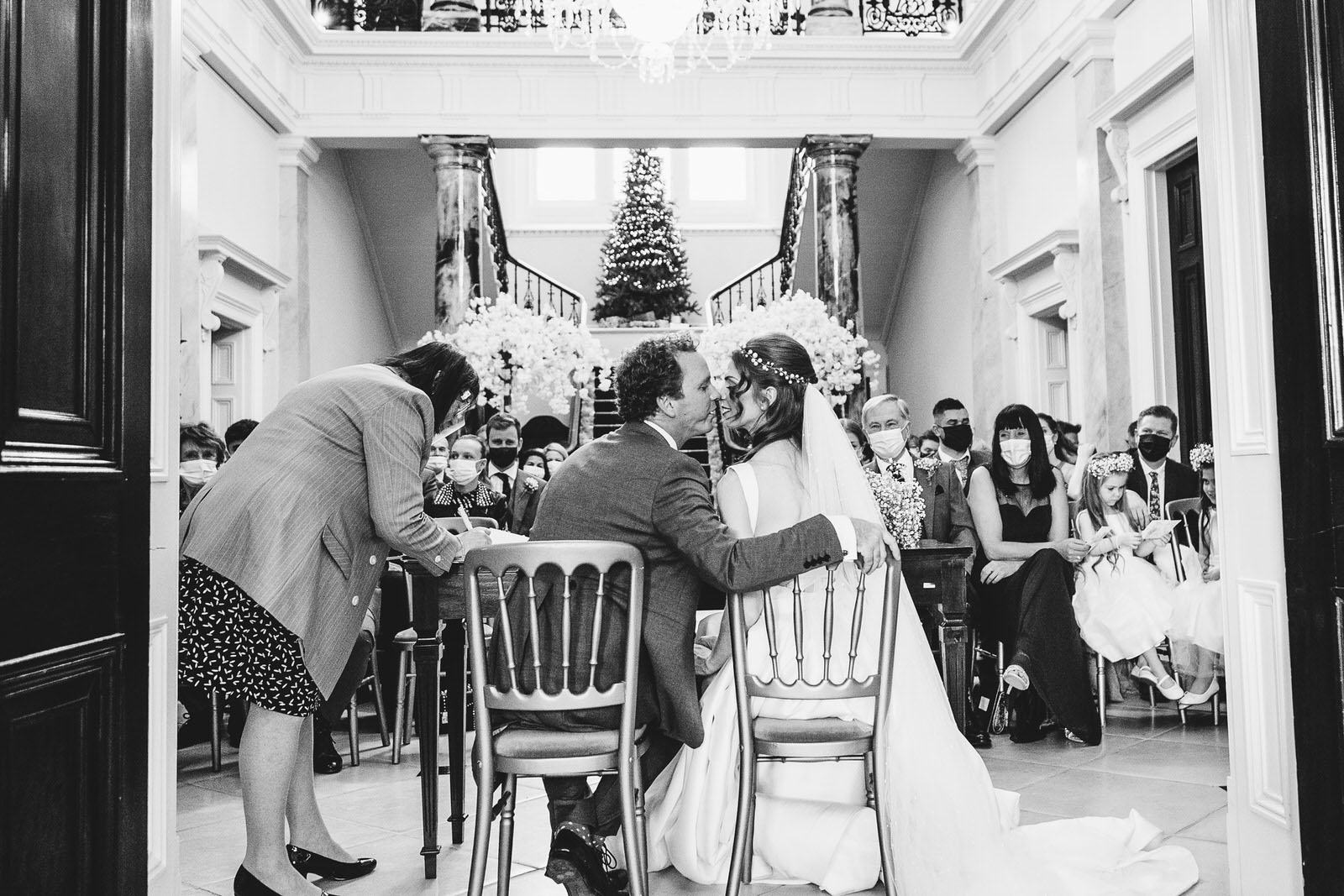 a bride and groom kissing in front of a christmas tree.