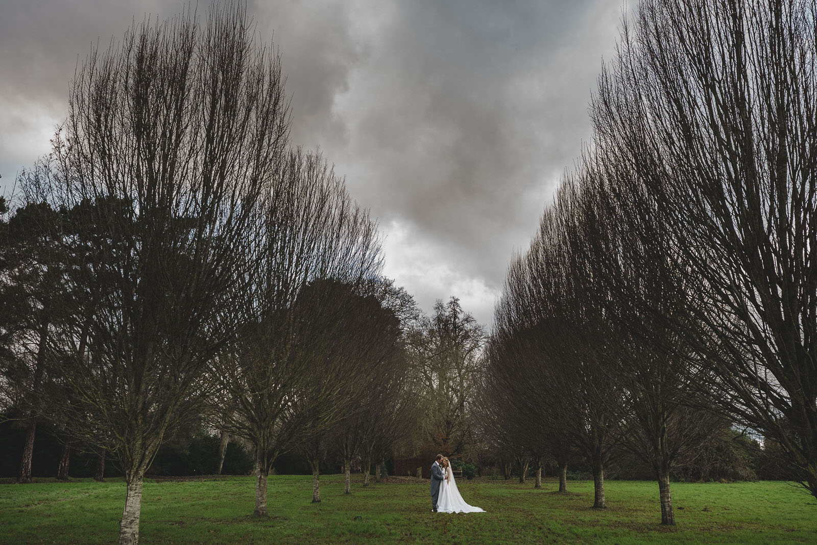 a bride and groom standing in a field under a cloudy sky.