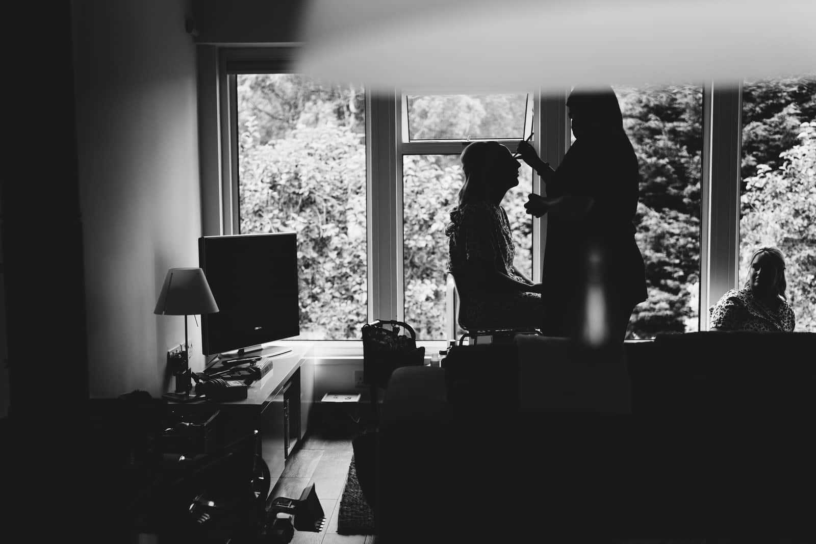 a black and white photo of a woman getting ready in front of a window.