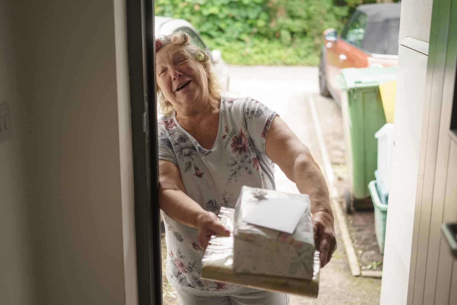 a woman is holding a package out of a door.