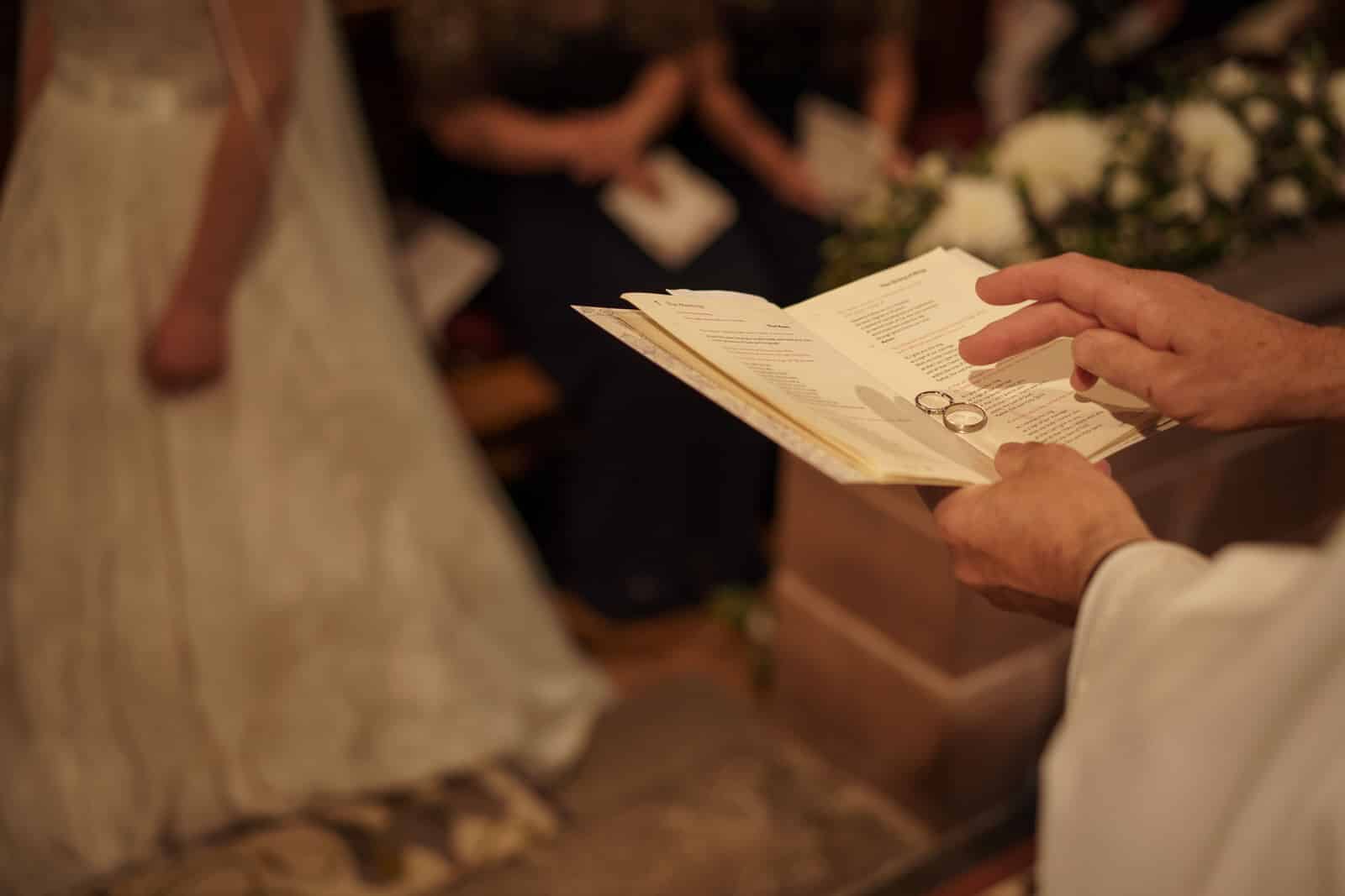 a man is holding a book in front of a bride and groom.