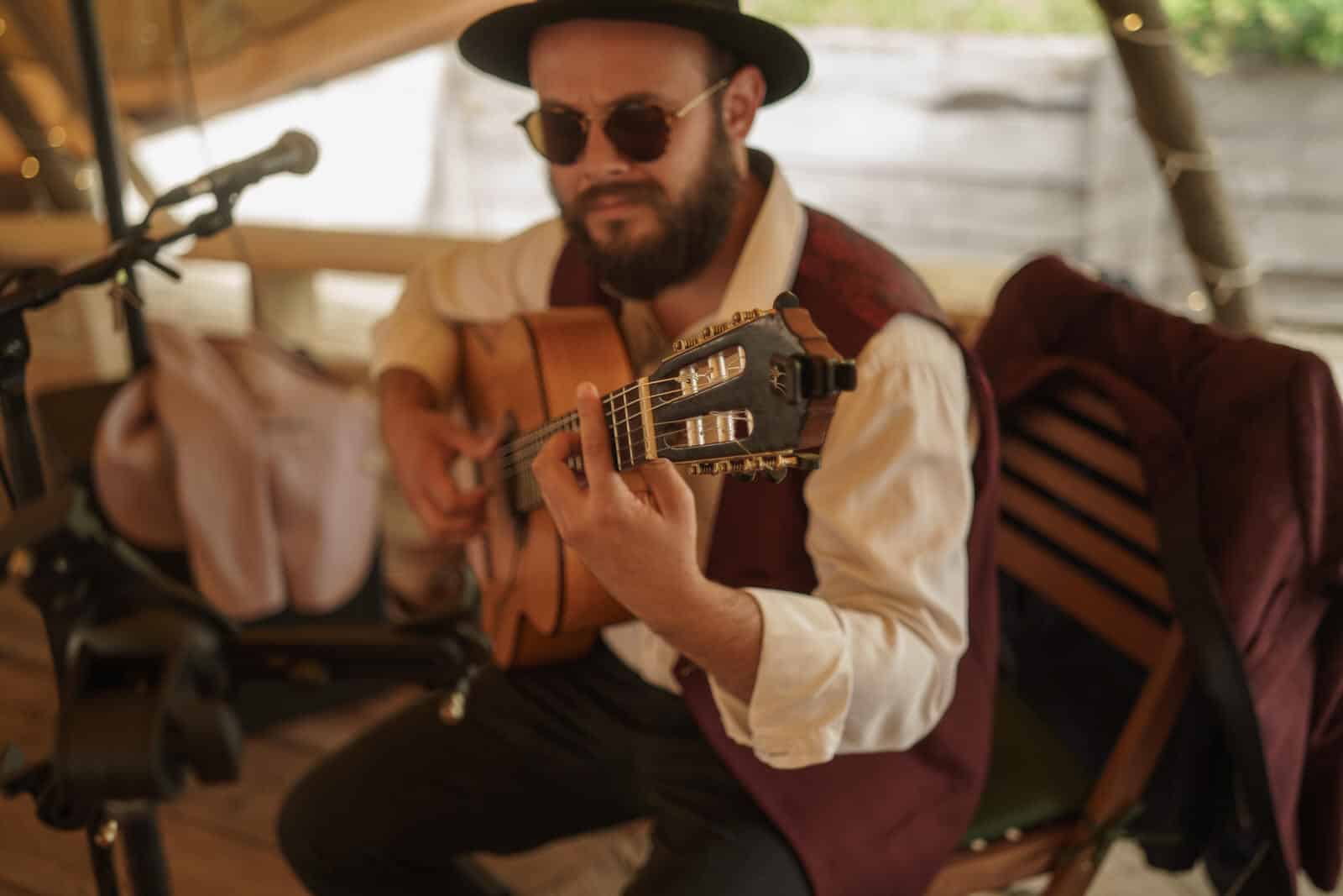 a man in a hat playing an acoustic guitar in a tent.