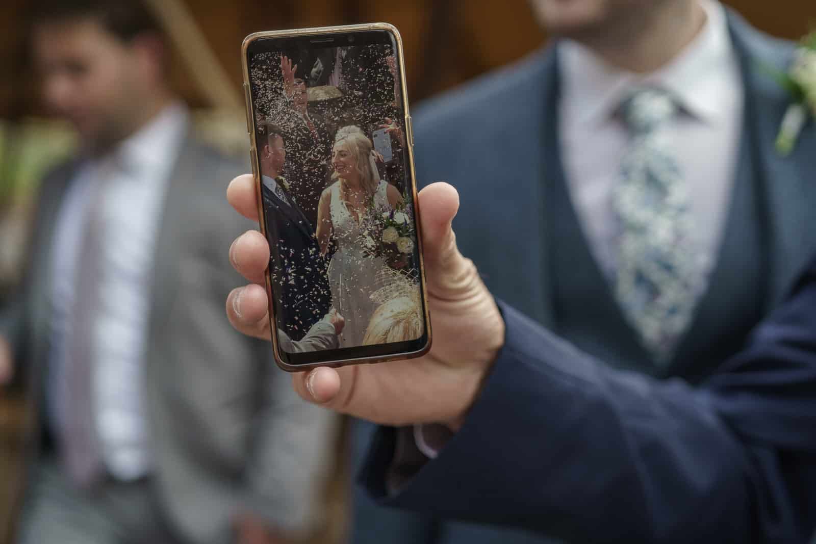 a man holding up a cell phone with a picture of a bride and groom.
