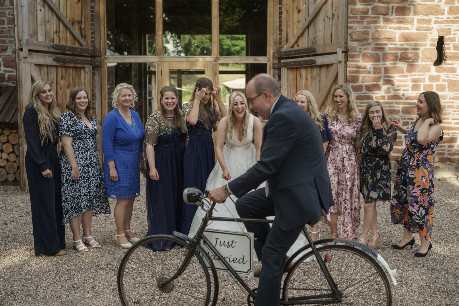 a group of bridesmaids pose with a bicycle in front of a barn.