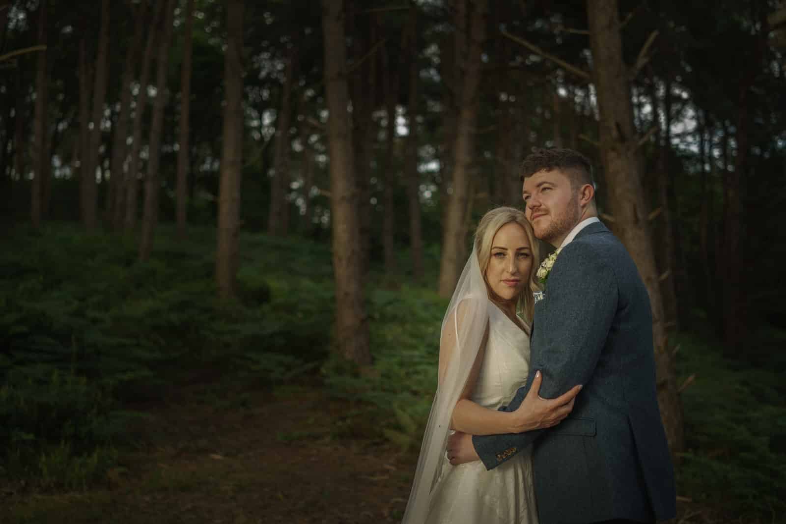 a bride and groom embracing in the woods.