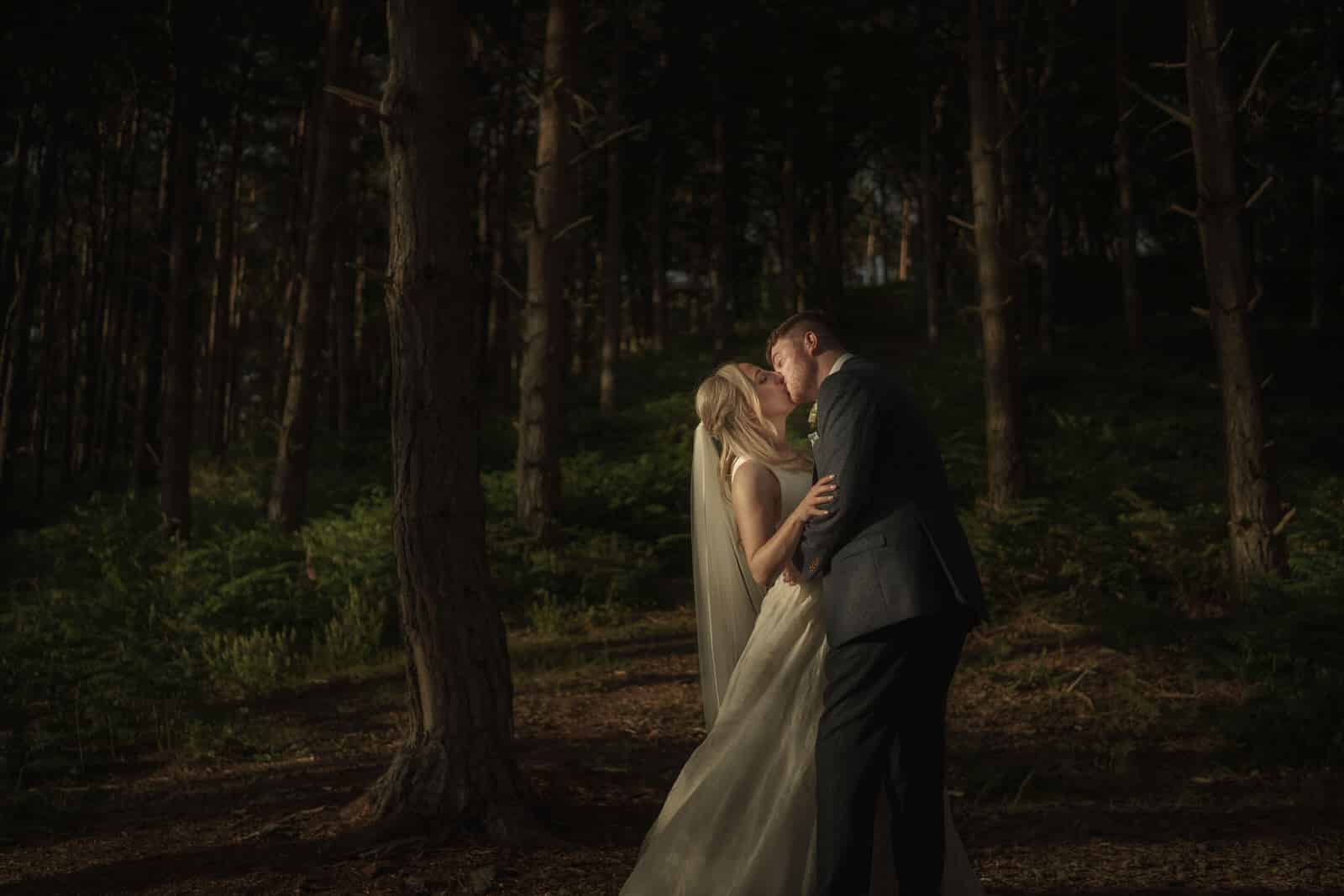 a bride and groom kissing in the woods.