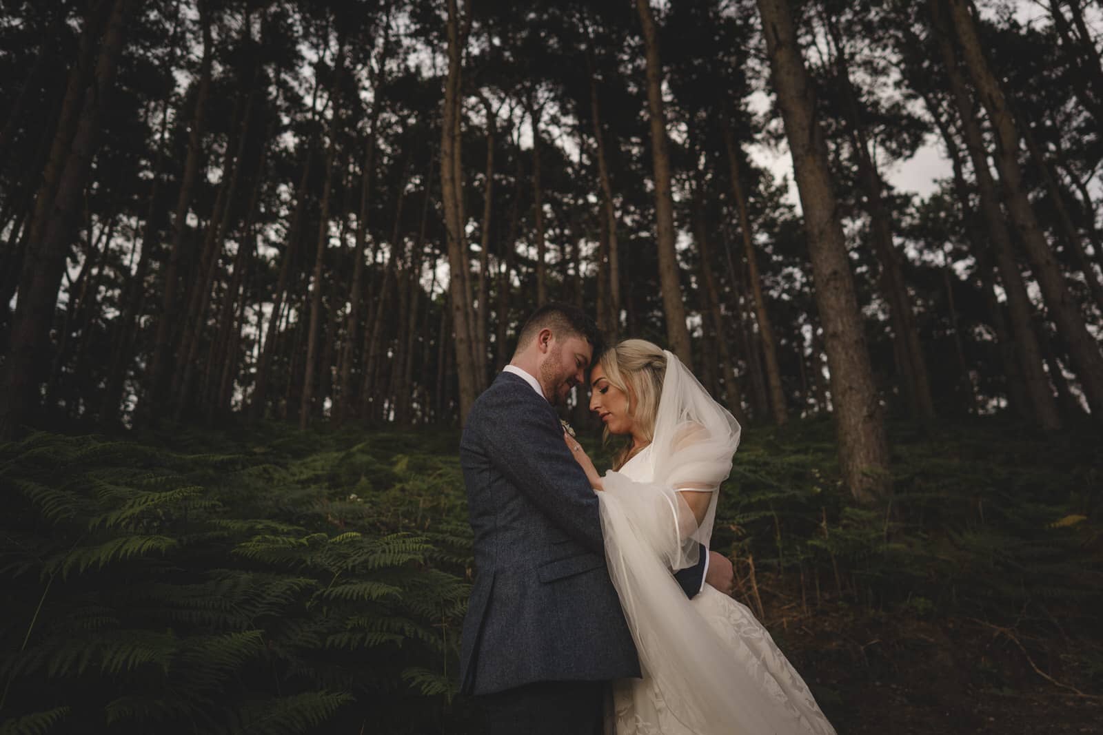 a bride and groom embrace in the woods.