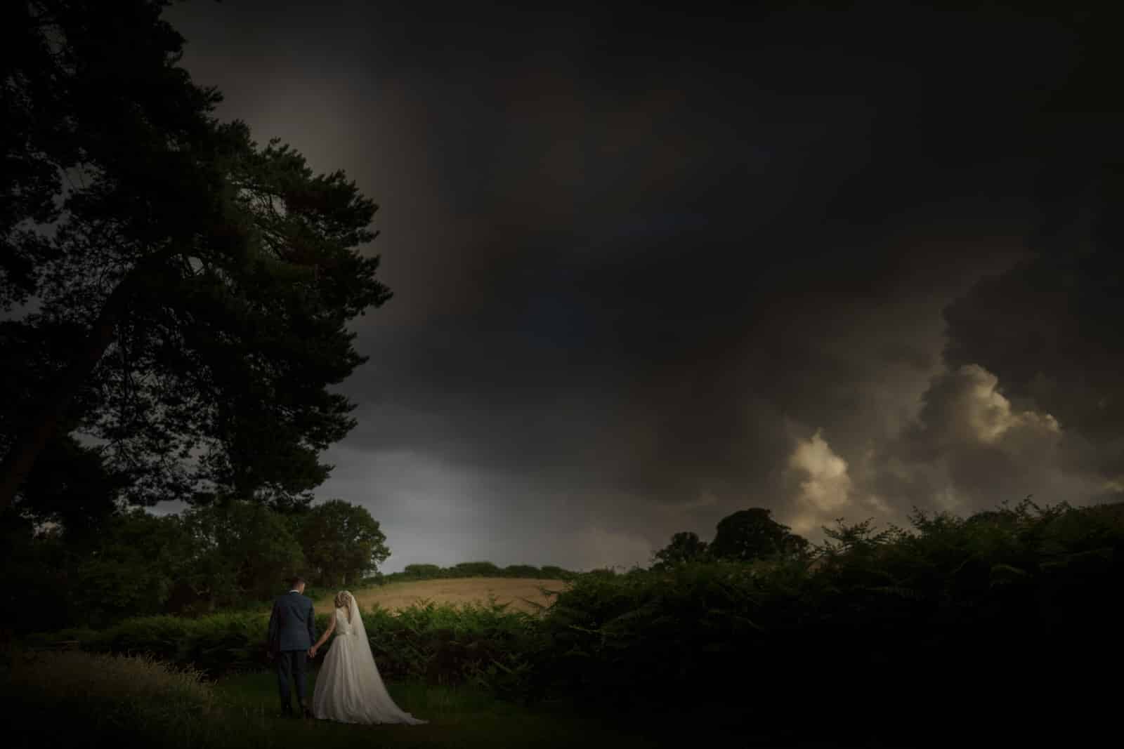 a bride and groom standing in a field under a stormy sky.