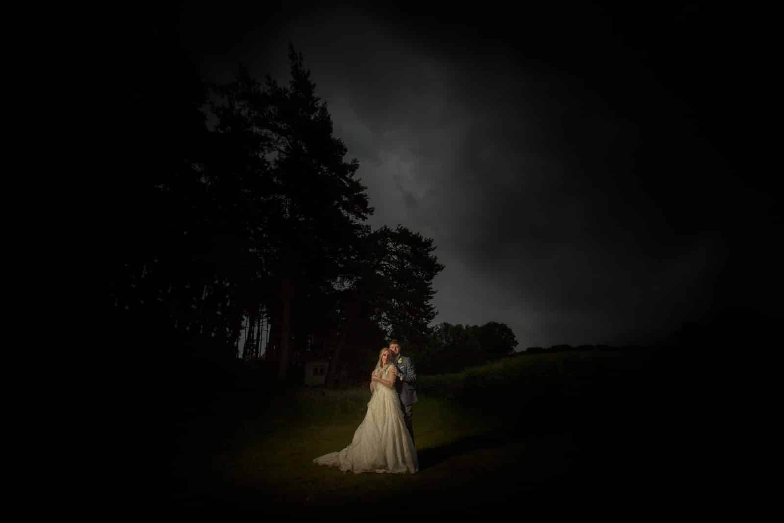 a bride and groom standing in the dark under a stormy sky.