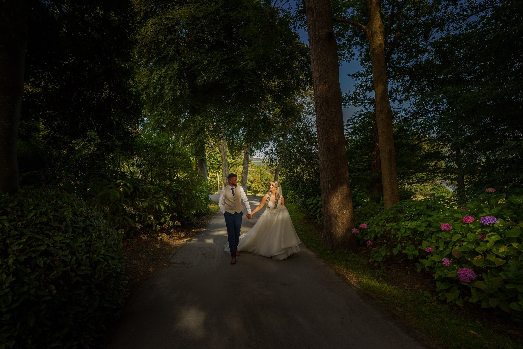 a bride and groom walking down a path in the woods.