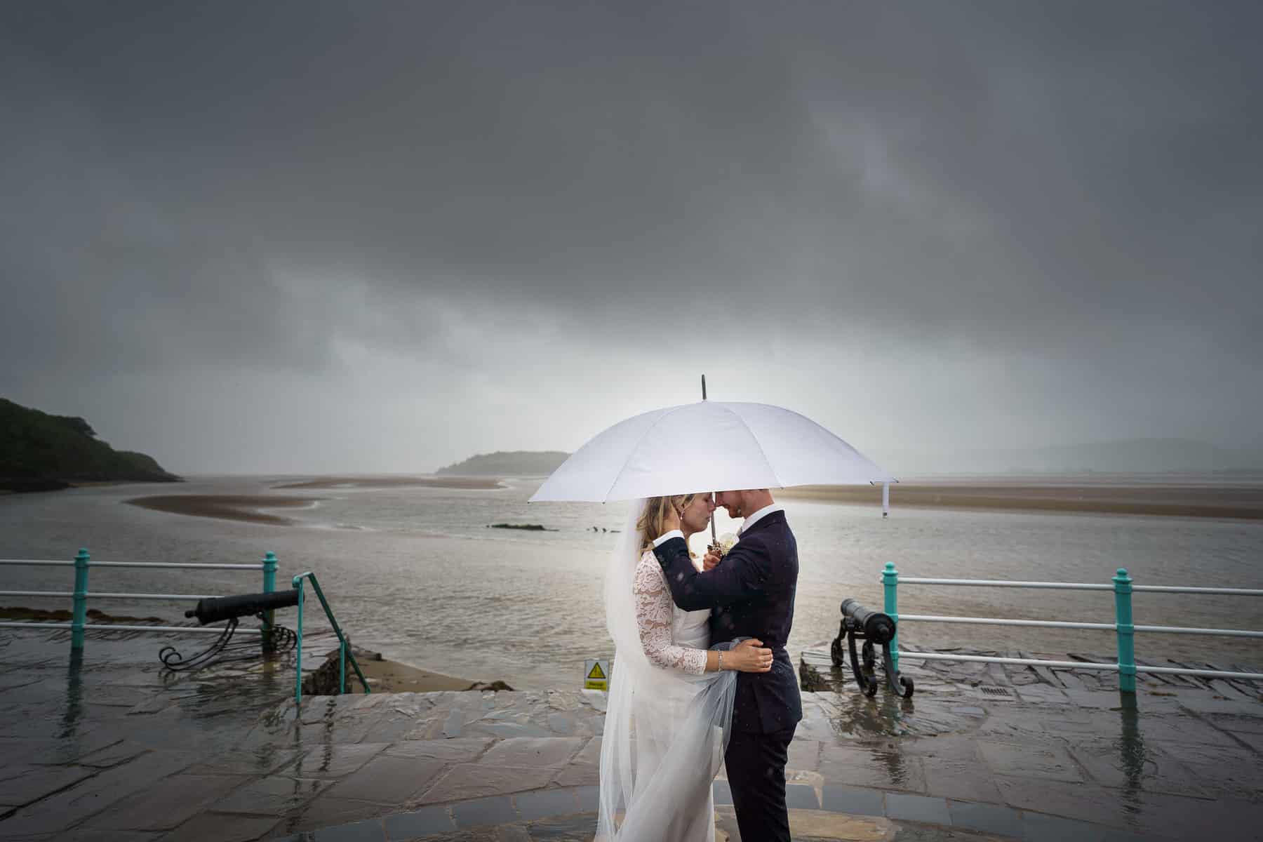 a bride and groom kiss under an umbrella in the rain.