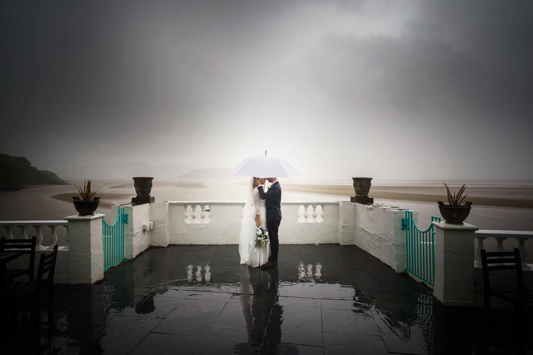 a bride and groom standing under an umbrella on a balcony.