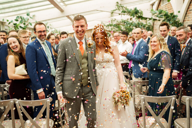 a bride and groom walk down the aisle with confetti thrown at them.