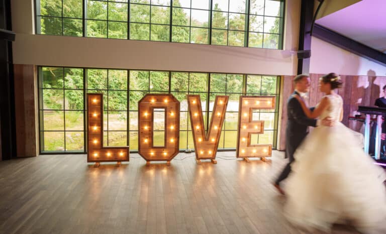 a bride and groom dancing in front of a large love sign at foxtail barns.