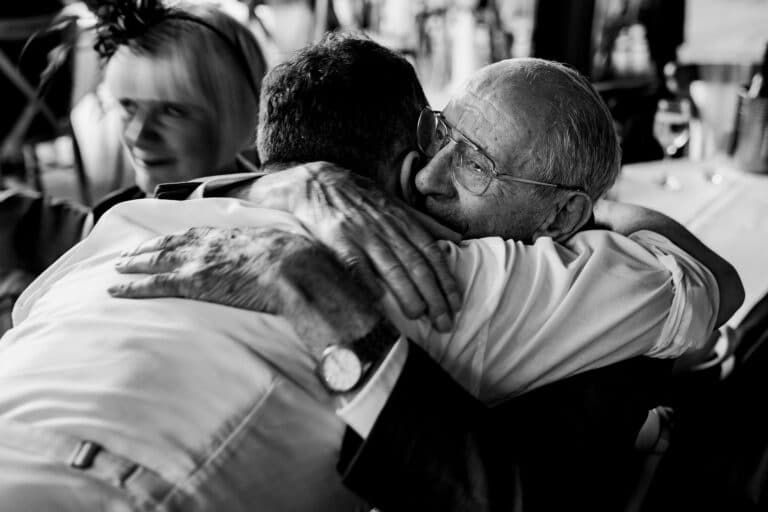 a man is hugging an older man at a wedding in the foxtail barns.