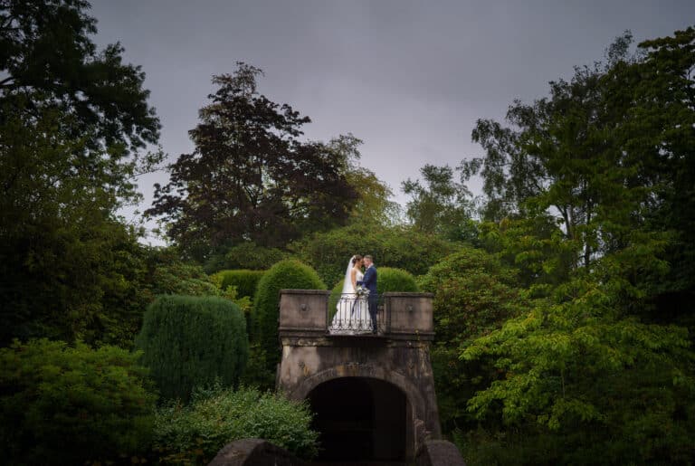 a bride and groom standing on a bridge in a foxtail barns garden.
