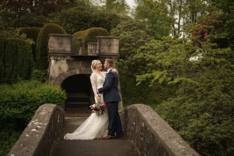 a bride and groom standing on a bridge at foxtail barns in a garden.