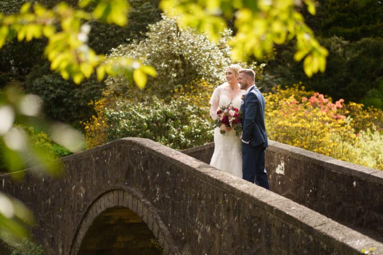 a bride and groom standing on a stone bridge in a garden at foxtail barns.