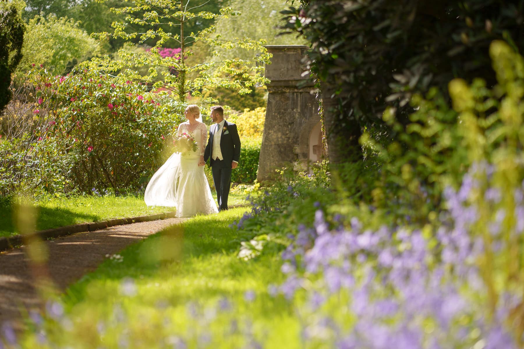 a bride and groom walking down a path in a garden surrounded by the beauty of foxtail barns.