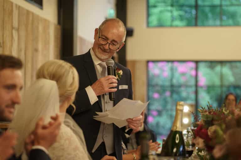 a man giving a heartfelt speech at a wedding reception held in the rustic ambiance of foxtail barns.