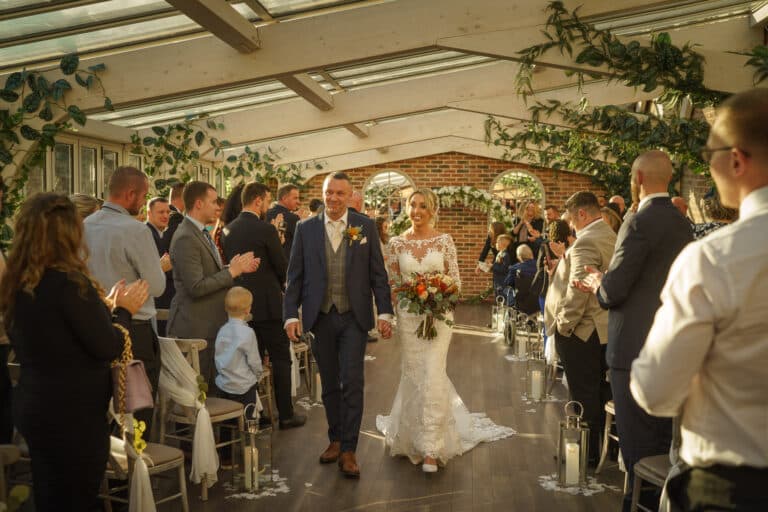 a bride and groom walking down the aisle in a foxtail barns greenhouse.