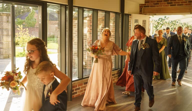 a group of brides and grooms walking down a hallway at foxtail barns.