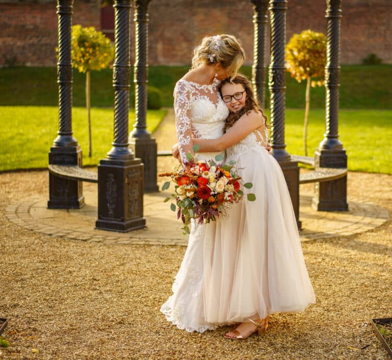 a bride and a little girl hugging in front of a foxtail barn.