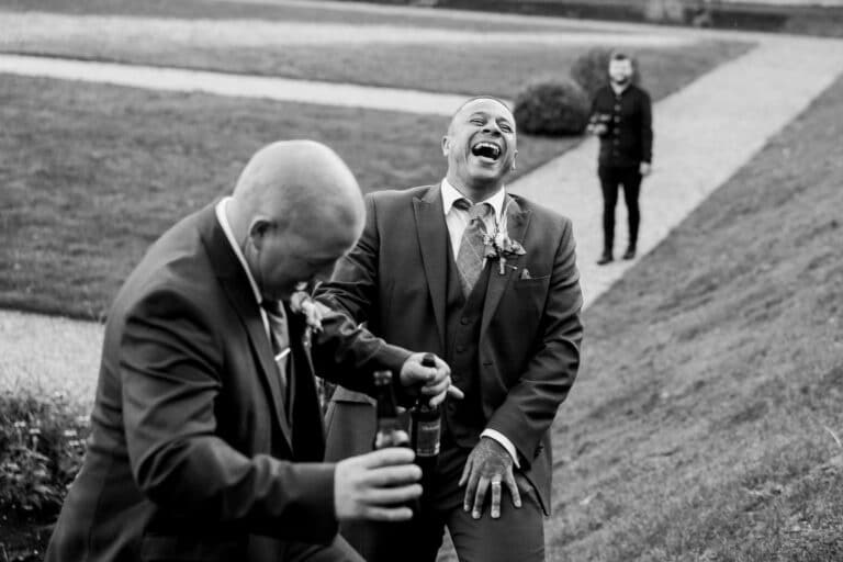 a black and white photo of a groom and groomsmen laughing at foxtail barns.