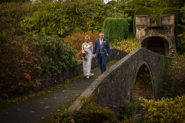 a bride and groom gracefully walk across a stone bridge at the enchanting foxtail barns venue.