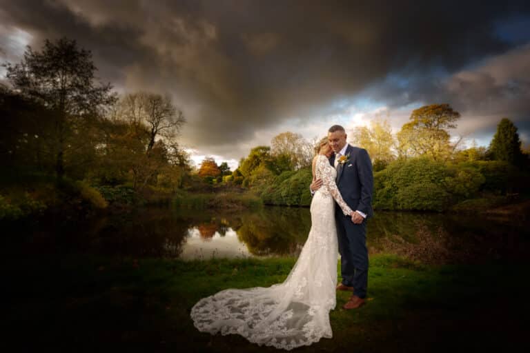 a bride and groom posing in front of a pond at foxtail barns.