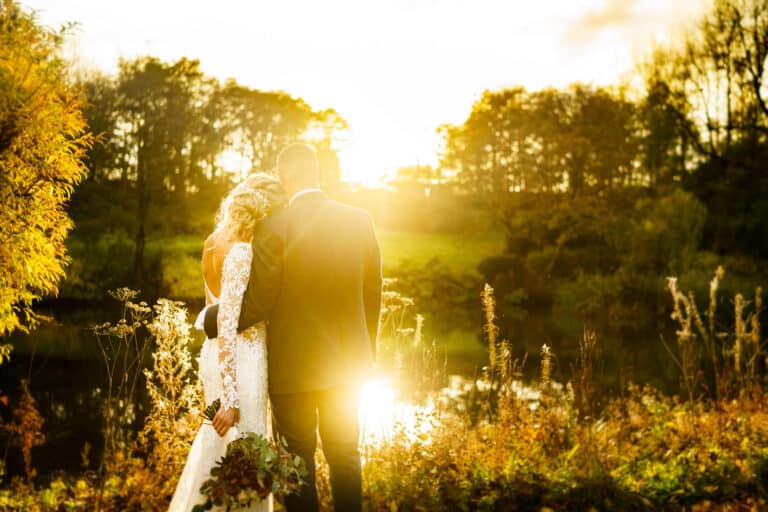 a bride and groom posing in front of a pond at sunset, with the picturesque backdrop of foxtail barns.