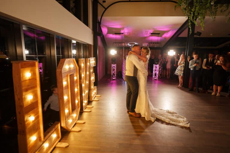 a bride and groom share their first dance at foxtail barns in front of illuminated letters.