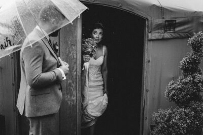 a bride and groom standing outside of a yurt on a rainy wedding day.