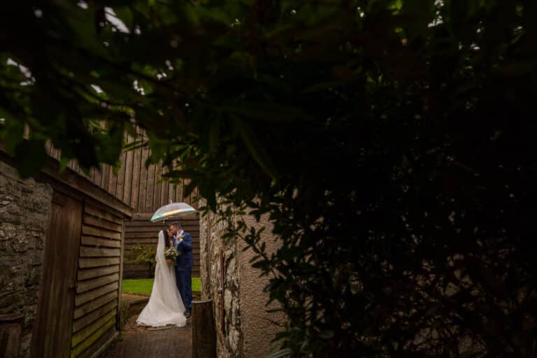 a bride and groom standing under an umbrella in an intimate courtyard.