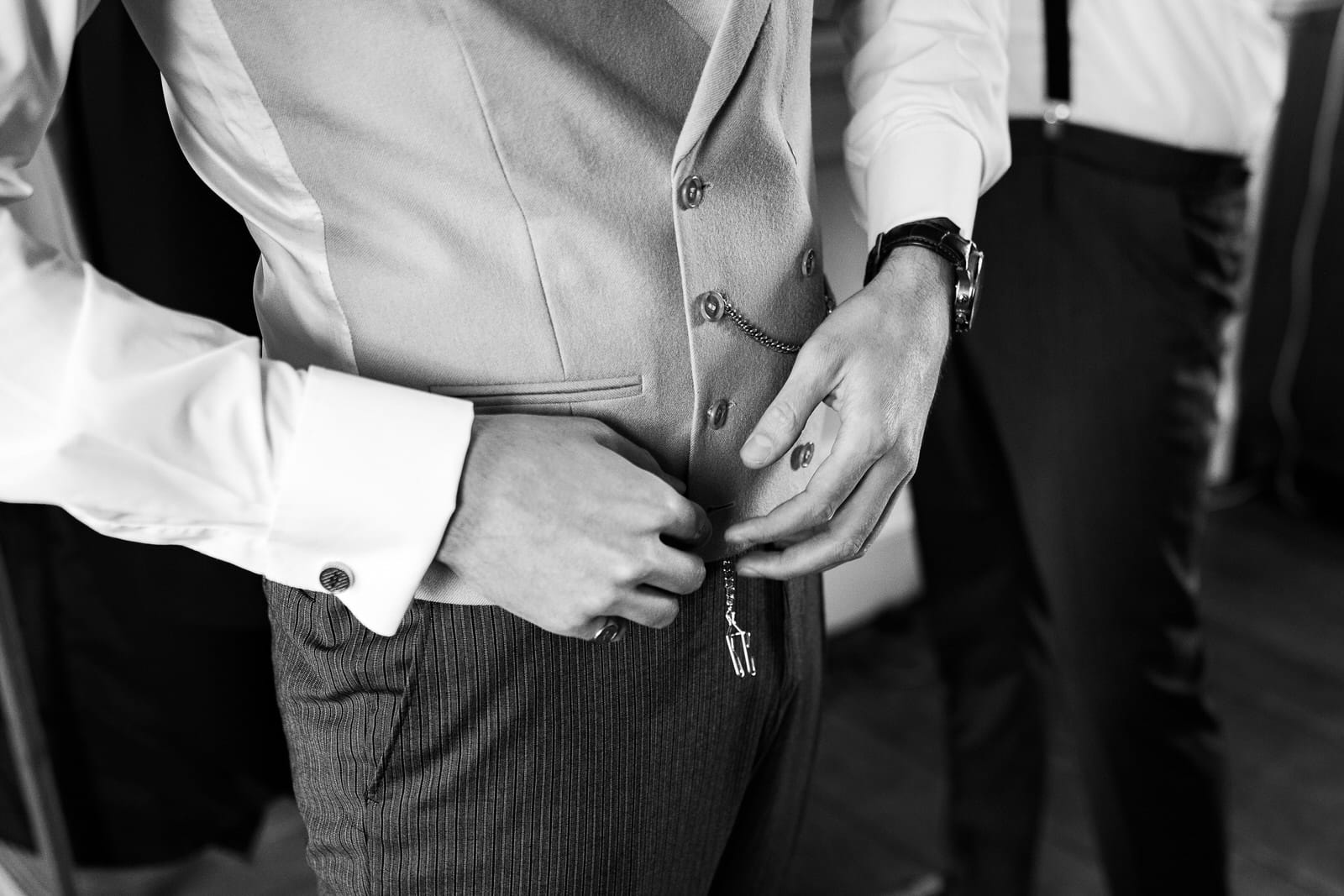 A person in a suit adjusts their vest buttons while another person, partially visible, stands nearby at Iscoyd Park in Shropshire.