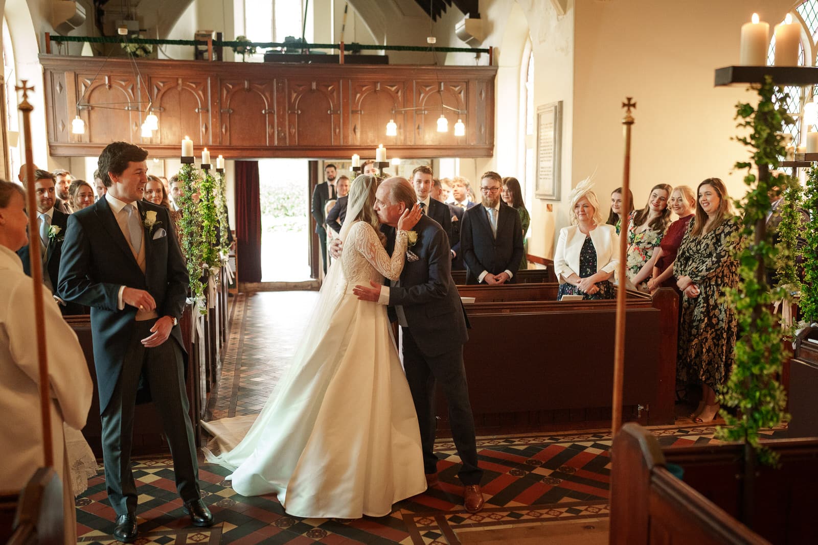a charming wedding unfolds as a couple shares a kiss at the altar of a decorated church during their ceremony, with guests seated and standing nearby.
