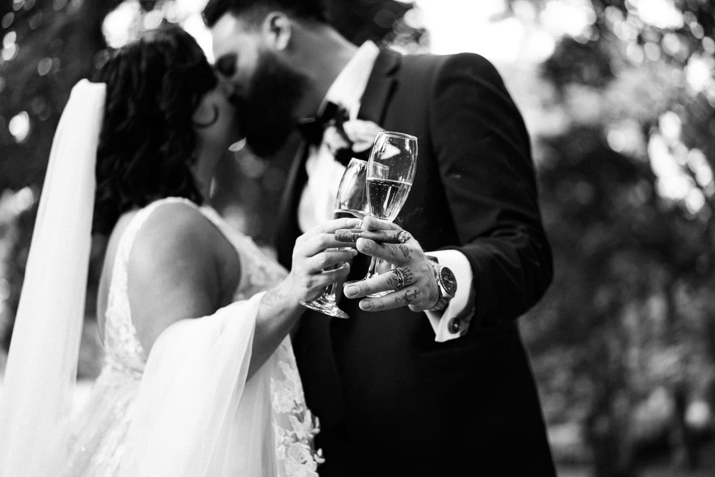 a couple in wedding attire shares a kiss, champagne glasses in hand, set against the backdrop of a grand castle wedding.