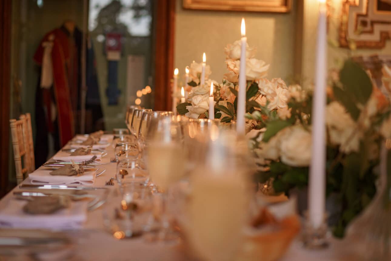 a long dining table set with glassware, silverware, white plates, white roses, and lit candles, prepared for a formal sandon hall wedding or elegant event.